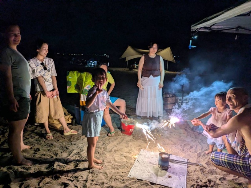 林崎松江海岸の夜に花火を囲んで笑顔を見せる多世代・多国籍のシェアメイト